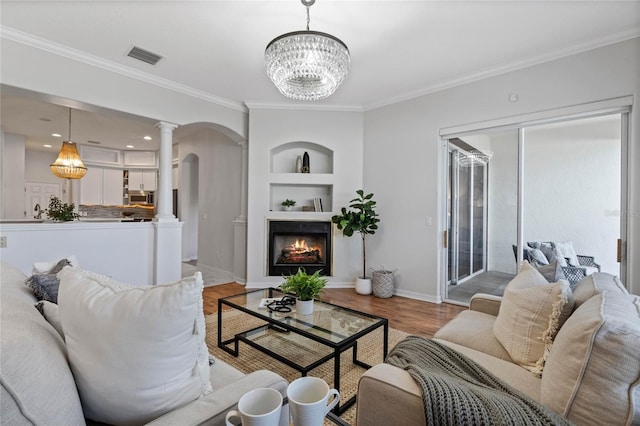 living room featuring decorative columns, built in features, ornamental molding, and light wood-type flooring