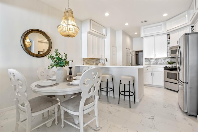 kitchen featuring white cabinets, stainless steel appliances, decorative backsplash, a kitchen breakfast bar, and hanging light fixtures