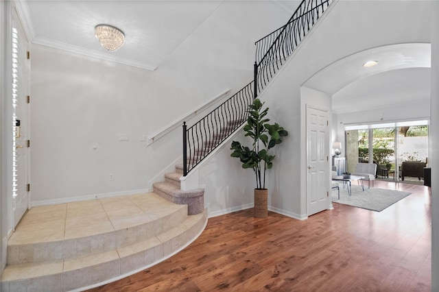 foyer entrance with wood-type flooring, crown molding, and vaulted ceiling