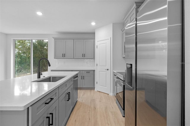 kitchen featuring gray cabinetry, sink, a center island with sink, light wood-type flooring, and stainless steel appliances