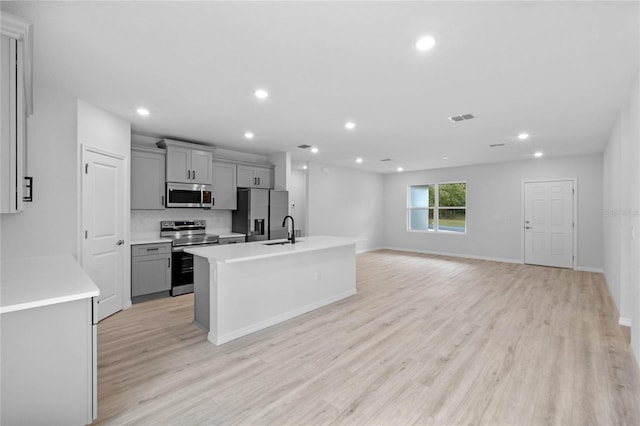 kitchen with gray cabinetry, sink, light hardwood / wood-style flooring, a kitchen island with sink, and appliances with stainless steel finishes