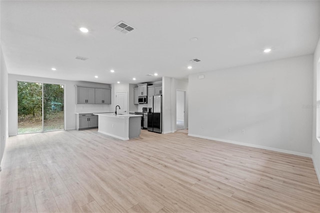 kitchen featuring gray cabinetry, sink, an island with sink, light hardwood / wood-style floors, and appliances with stainless steel finishes