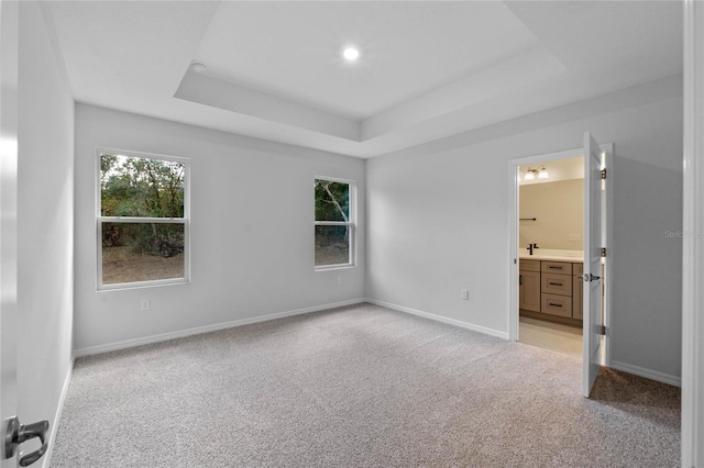 unfurnished bedroom featuring connected bathroom, a raised ceiling, and light carpet