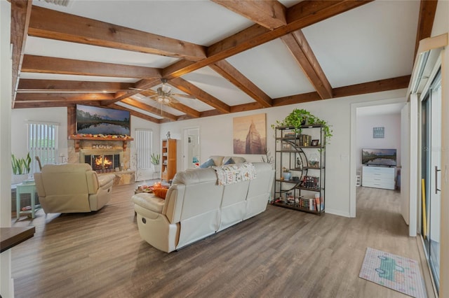 living room with a stone fireplace, hardwood / wood-style floors, vaulted ceiling with beams, and ceiling fan