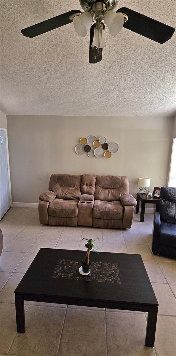 living room with ceiling fan, light tile patterned floors, and a textured ceiling