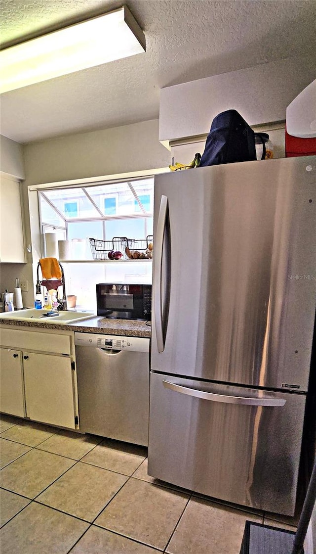 kitchen with white cabinets, light tile patterned floors, stainless steel appliances, and a textured ceiling