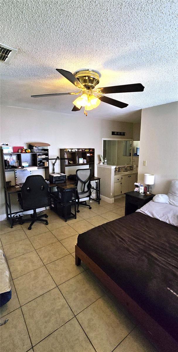 tiled bedroom with ceiling fan and a textured ceiling