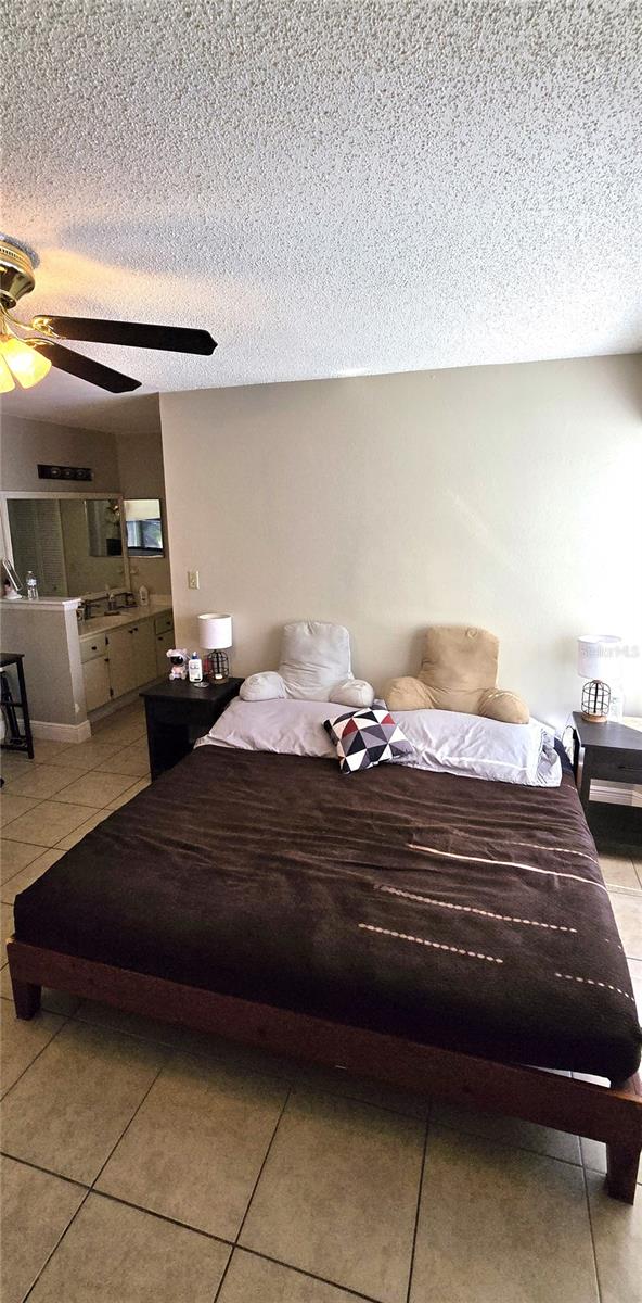 bedroom featuring ceiling fan, light tile patterned flooring, and a textured ceiling