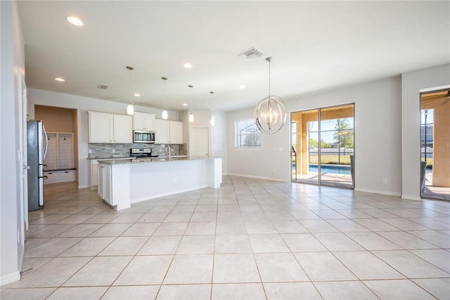 kitchen with a kitchen island with sink, white cabinets, hanging light fixtures, tasteful backsplash, and stainless steel appliances