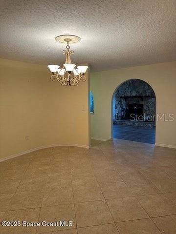 tiled spare room with a textured ceiling and a chandelier