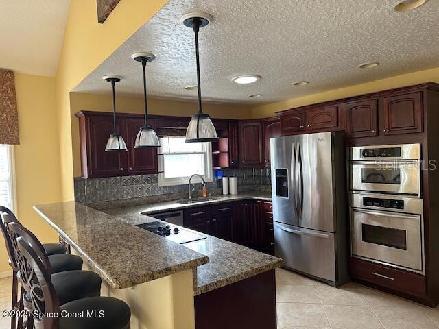 kitchen with sink, appliances with stainless steel finishes, a kitchen breakfast bar, decorative light fixtures, and kitchen peninsula