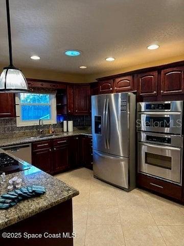 kitchen with appliances with stainless steel finishes, pendant lighting, sink, decorative backsplash, and dark stone counters