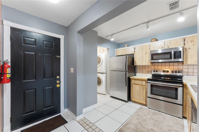 kitchen with stainless steel appliances, a textured ceiling, stacked washer / dryer, rail lighting, and light tile patterned flooring