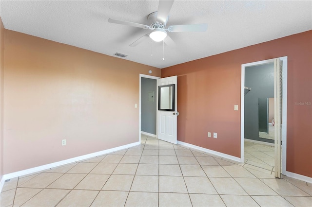 unfurnished bedroom with a textured ceiling, a spacious closet, ceiling fan, and light tile patterned floors