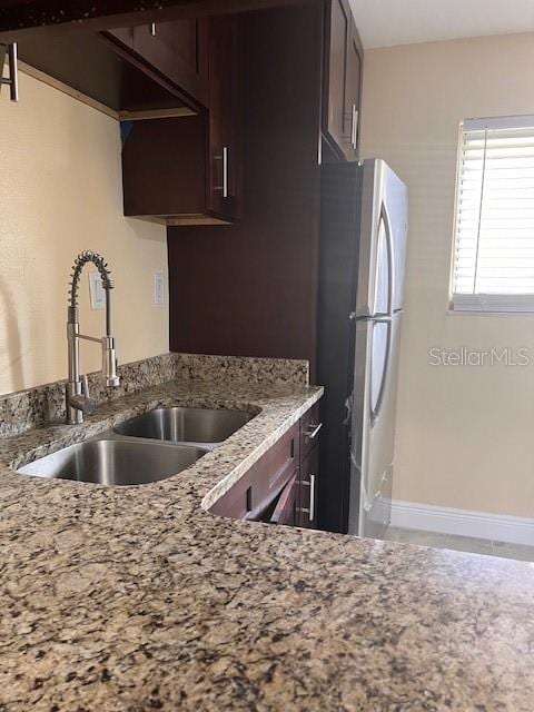 kitchen with light stone countertops, dark brown cabinetry, sink, and stainless steel fridge