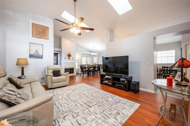 living room with hardwood / wood-style floors, a tile fireplace, high vaulted ceiling, ceiling fan with notable chandelier, and a skylight