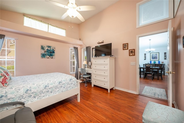 bedroom with hardwood / wood-style floors, ceiling fan with notable chandelier, and a high ceiling