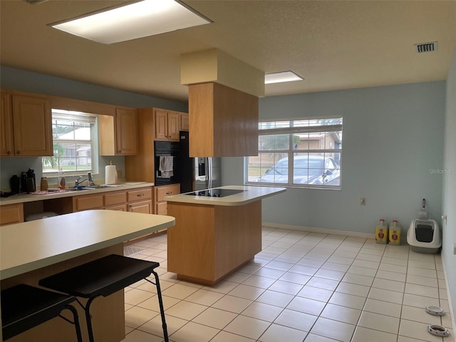 kitchen featuring light tile patterned floors, light brown cabinetry, sink, a breakfast bar, and a center island