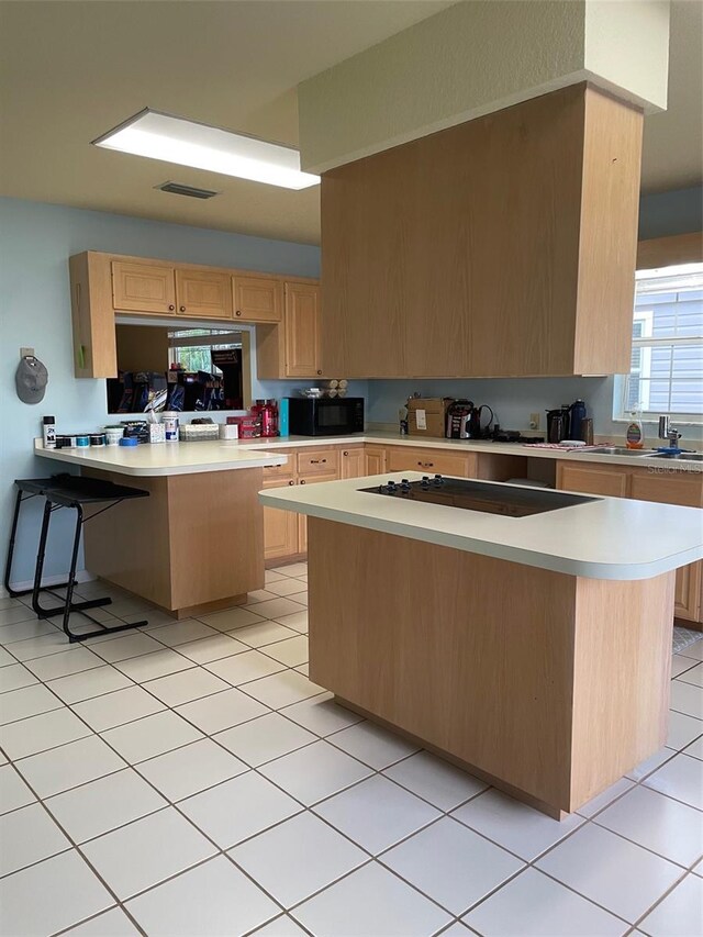 kitchen with light tile patterned flooring, black appliances, kitchen peninsula, light brown cabinets, and a breakfast bar area