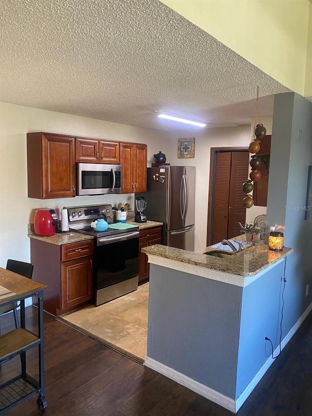 kitchen featuring a textured ceiling, kitchen peninsula, stainless steel appliances, and light hardwood / wood-style flooring