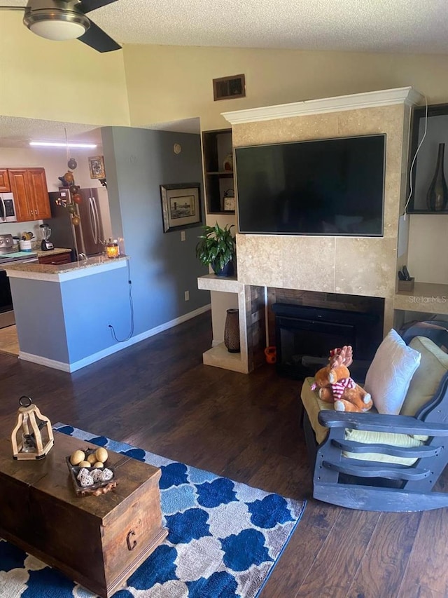 living room featuring ceiling fan, dark wood-type flooring, a textured ceiling, vaulted ceiling, and a tiled fireplace