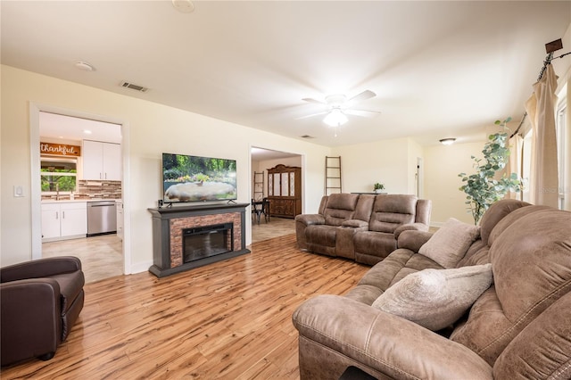 living room with a stone fireplace, ceiling fan, sink, and light wood-type flooring