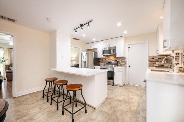 kitchen with kitchen peninsula, tasteful backsplash, a breakfast bar, stainless steel appliances, and white cabinetry