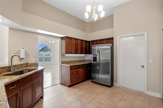 kitchen with light stone counters, an inviting chandelier, stainless steel refrigerator with ice dispenser, sink, and pendant lighting