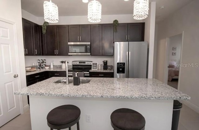 kitchen with decorative light fixtures, stainless steel appliances, dark brown cabinets, and a center island with sink