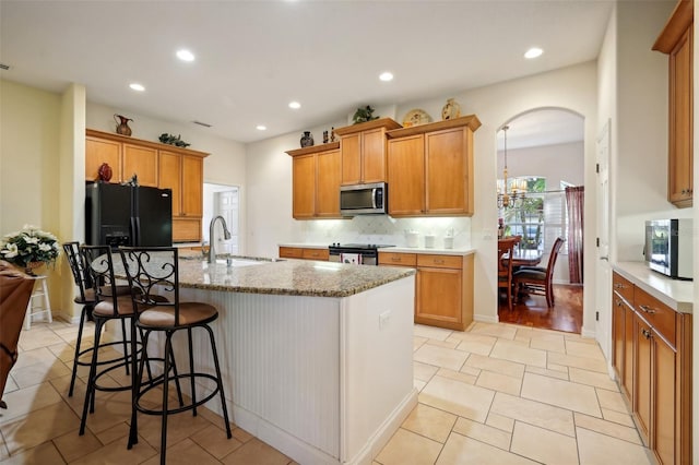 kitchen featuring appliances with stainless steel finishes, a kitchen island with sink, light tile patterned floors, sink, and backsplash