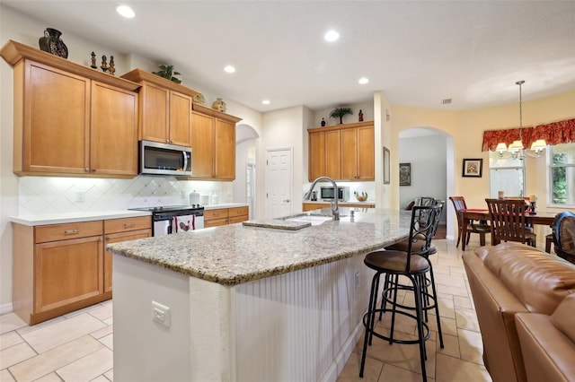 kitchen featuring appliances with stainless steel finishes, decorative light fixtures, decorative backsplash, sink, and a center island with sink