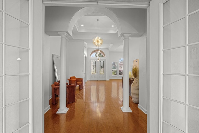 hallway with wood-type flooring, ornate columns, a raised ceiling, and ornamental molding