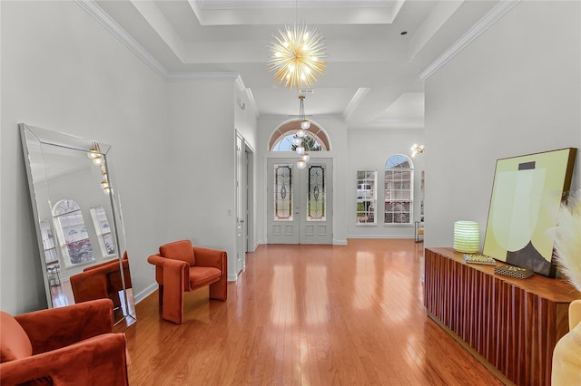 entryway with a tray ceiling, light hardwood / wood-style flooring, ornamental molding, and a notable chandelier