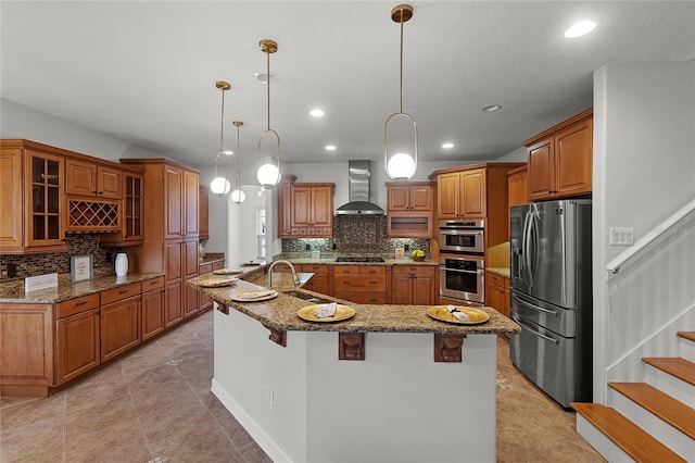 kitchen with a breakfast bar, appliances with stainless steel finishes, decorative light fixtures, and wall chimney range hood