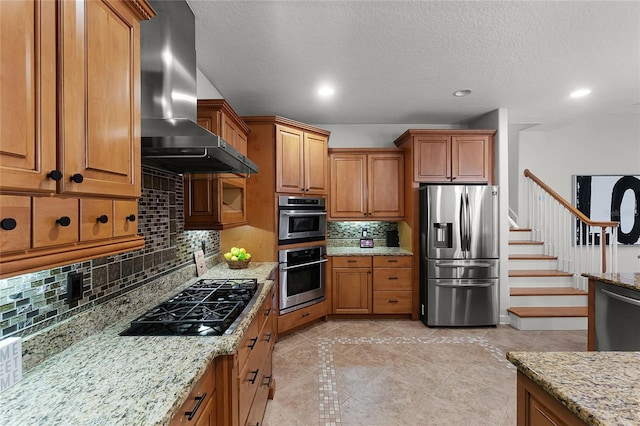 kitchen featuring light stone counters, wall chimney range hood, appliances with stainless steel finishes, and tasteful backsplash