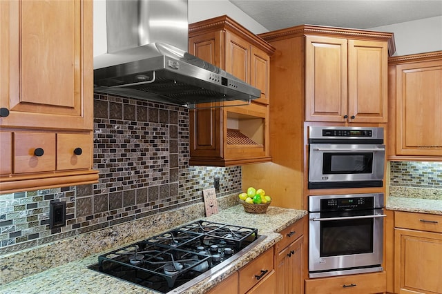 kitchen with decorative backsplash, light stone counters, black gas stovetop, and wall chimney range hood