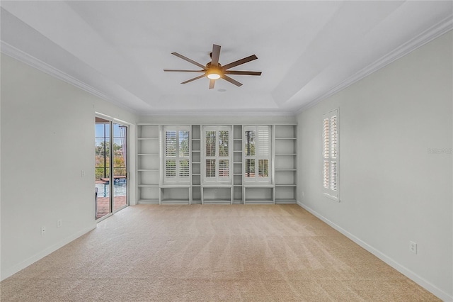 spare room with built in shelves, ceiling fan, crown molding, a tray ceiling, and light carpet