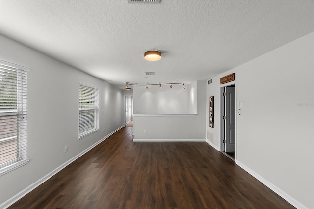 unfurnished room featuring rail lighting, dark hardwood / wood-style floors, plenty of natural light, and a textured ceiling