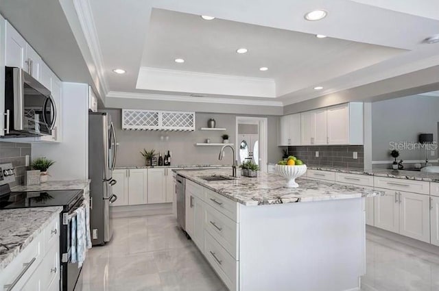 kitchen with sink, tasteful backsplash, a raised ceiling, an island with sink, and appliances with stainless steel finishes