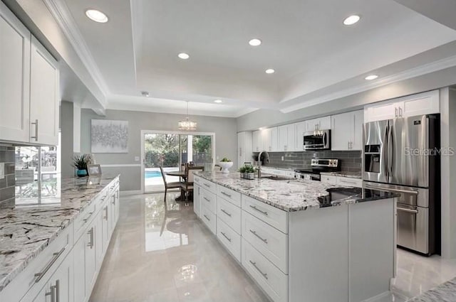 kitchen with tasteful backsplash, stainless steel appliances, a kitchen island with sink, sink, and white cabinetry