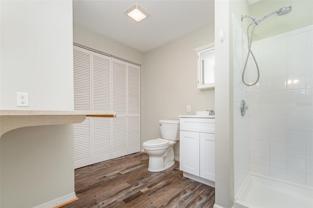 bathroom with hardwood / wood-style floors, vanity, a tile shower, and toilet