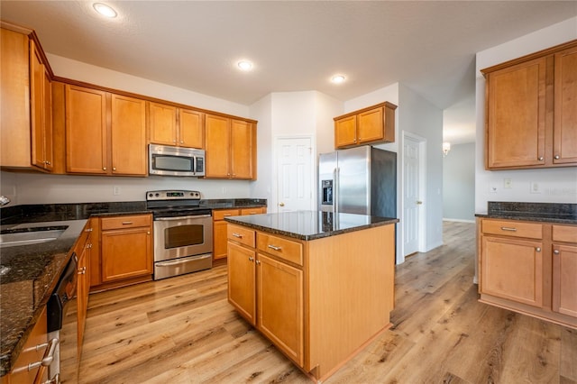 kitchen with dark stone counters, a kitchen island, light wood-type flooring, and appliances with stainless steel finishes