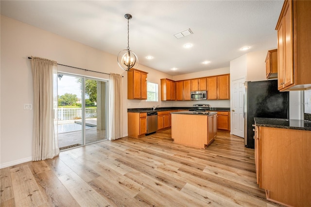 kitchen with sink, appliances with stainless steel finishes, pendant lighting, a kitchen island, and light wood-type flooring