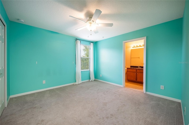 unfurnished bedroom featuring ensuite bath, ceiling fan, light colored carpet, a textured ceiling, and a closet