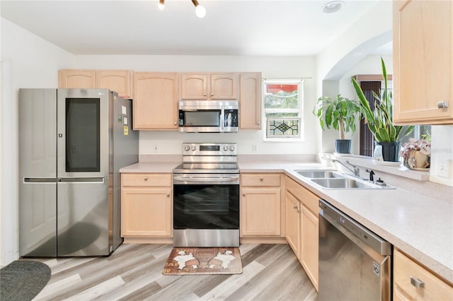 kitchen with stainless steel appliances, light brown cabinetry, sink, and light hardwood / wood-style flooring