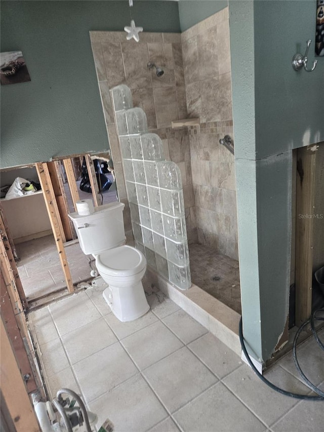 bathroom featuring tile patterned flooring, a tile shower, and toilet