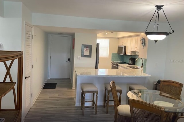 kitchen featuring pendant lighting, dark hardwood / wood-style floors, white cabinetry, kitchen peninsula, and stainless steel appliances