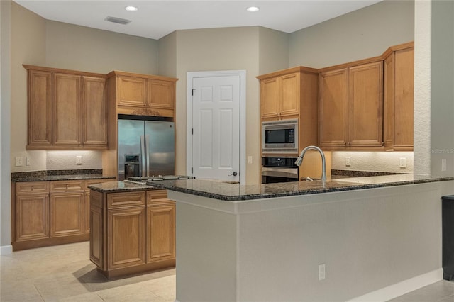 kitchen with dark stone countertops, kitchen peninsula, appliances with stainless steel finishes, and light tile patterned flooring