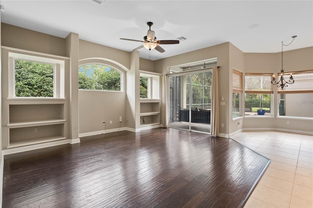 empty room with hardwood / wood-style floors, built in features, and ceiling fan with notable chandelier