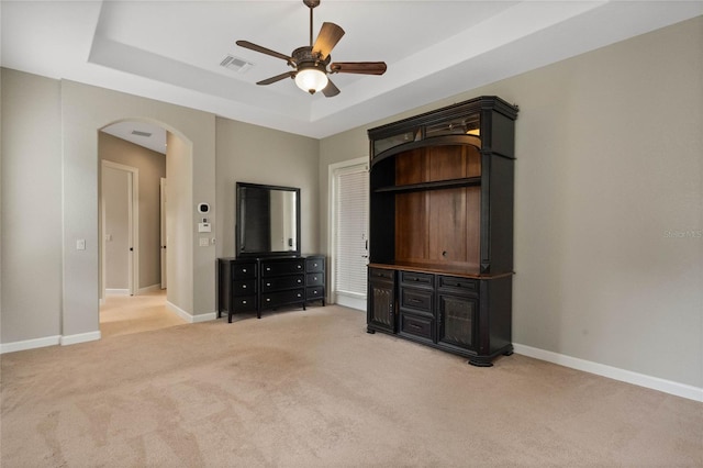 unfurnished bedroom featuring light carpet, ceiling fan, and a raised ceiling